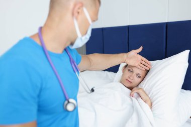 Doktor hasta bir kadının alnına elini koyuyor.