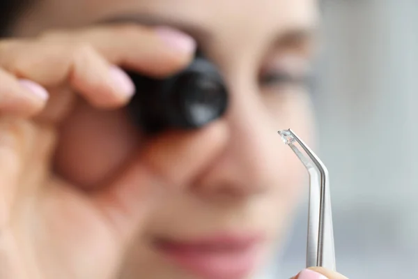 Jewelut looks through magnifying glass at gem in tweezers closeup — Stock Photo, Image