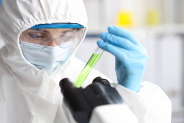 Koruyucu kıyafetli ve maskeli bilim adamları test tüplerini yakın tutuyor.