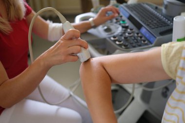 Doktor, klinikte hastanın dirseğini ultrason ile muayene ediyor.