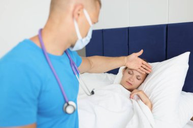 Üniformalı erkek doktor yatakta yatan hastanın sıcaklığını kontrol ediyor.