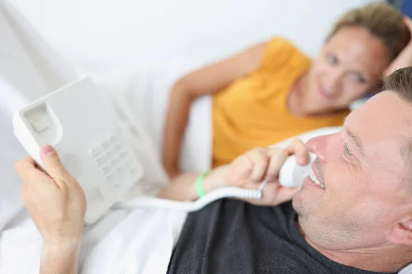 Sonriente pareja casada llama por teléfono mientras está acostado en la cama en los hoteles —  Fotos de Stock