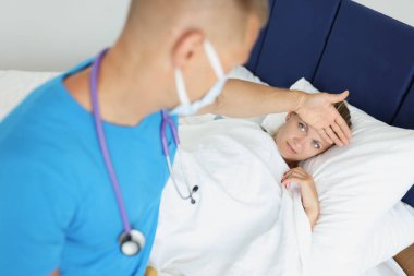 Doktor yatakta hasta bir kadının alnına dokunuyor.