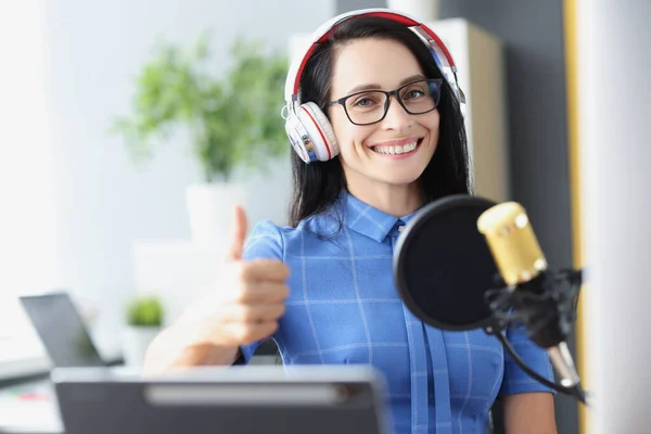 Woman radio host in headphones with microphone holds thumbs up — стоковое фото