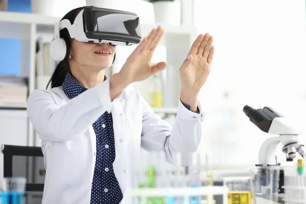 Молодая женщина-врач в наушниках виртуальной реальности работает на компьютере в больничном кабинете — стоковое фото