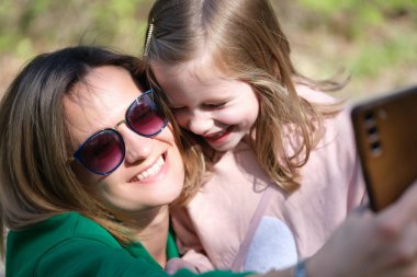 Çocuklu genç bir kadın parkta cep telefonuyla selfie çekiyor.