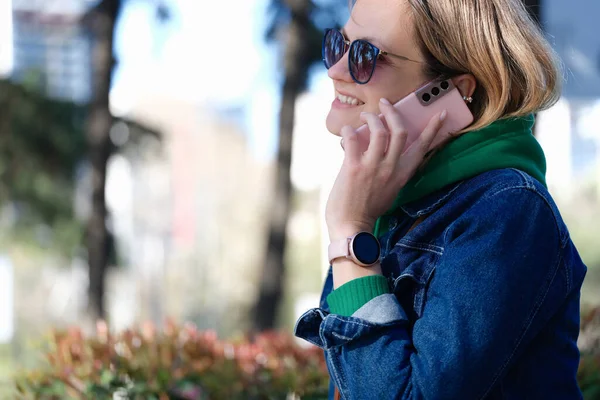 Γυναίκα με γυαλιά ηλίου χαμογελώντας και μιλώντας στο κινητό τηλέφωνο στο πάρκο — Φωτογραφία Αρχείου