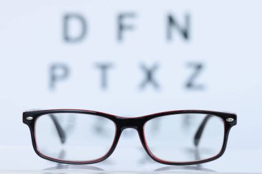 Göz testi masasının arka planında duran siyah çerçeveli gözlüklerName