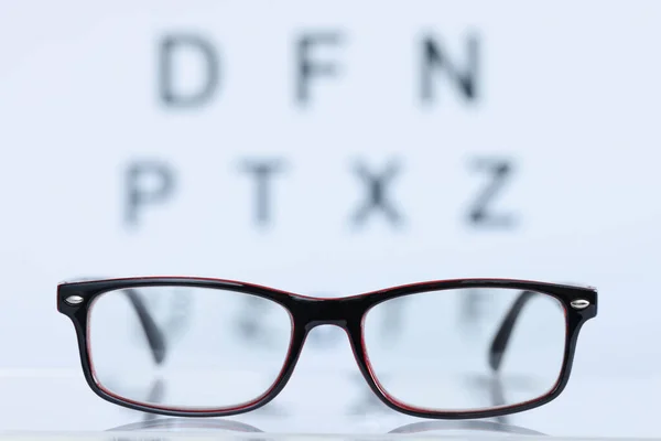 Göz testi masasının arka planında duran siyah çerçeveli gözlüklerName — Stok fotoğraf