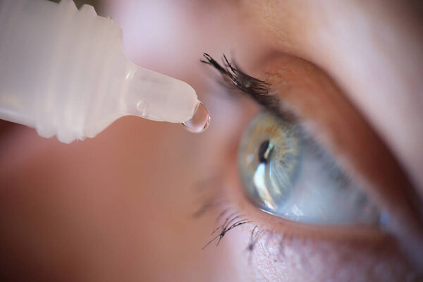 Woman dripping drops from plastic bottle into her eyes closeup