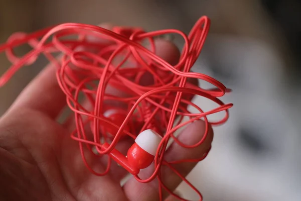 Tangled red headphones in hand closeup. Person trying to unravel broken headphones — стоковое фото