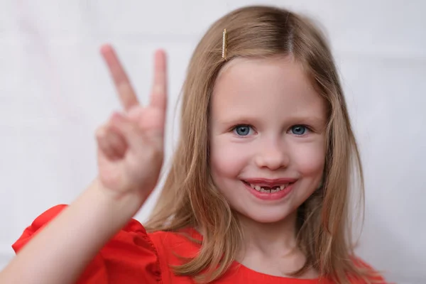 Smiling little girl without front teeth gesture two fingers up — Fotografia de Stock