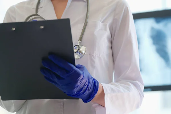 Radiologist checks x-ray image and holds clipboard in hands — Stock fotografie