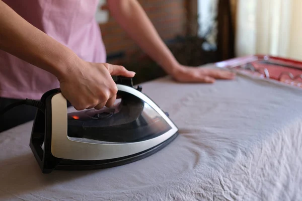Woman with iron in hands irons clothes on ironing board — Stock Fotó