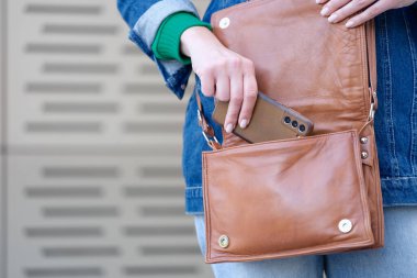 Young woman putting modern smartphone in bag
