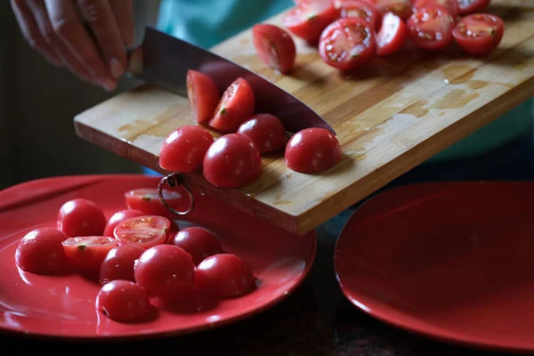 Woman cutting tomatoes on wooden board and and putting on plate — Stockfoto