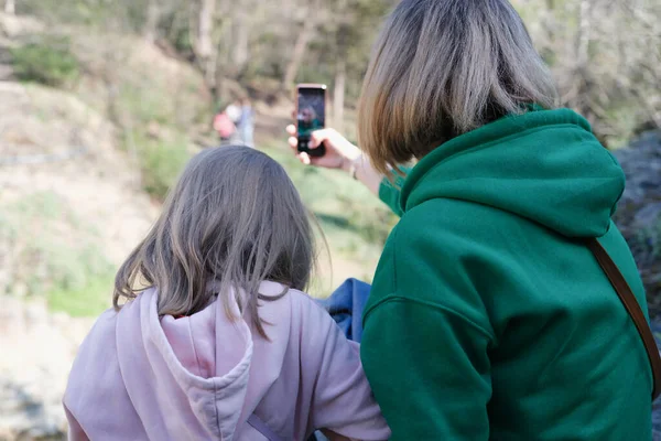 Mom and daughter sit with backs and take pictures of nature on smartphone — Stock Photo, Image