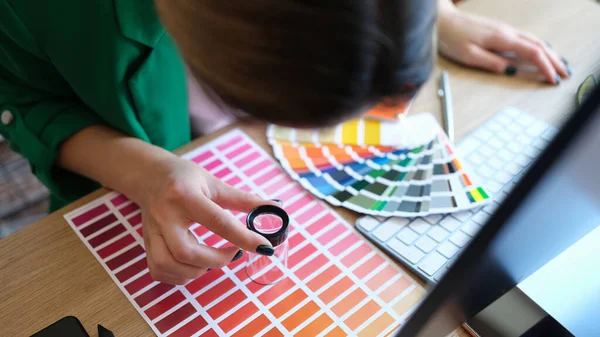 Designer olha através de lupa em amostras de cores e tons de vermelho na paleta de papel — Fotografia de Stock