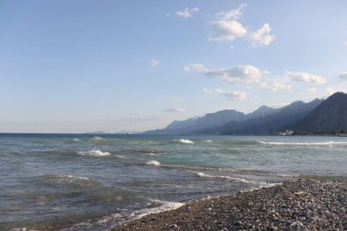 Bulutlu mavi arkaplanlı çakıl taşı plajına yakın çekim. Dağ manzarası. Resimli deniz kıyısı. Yaz zamanı konsepti