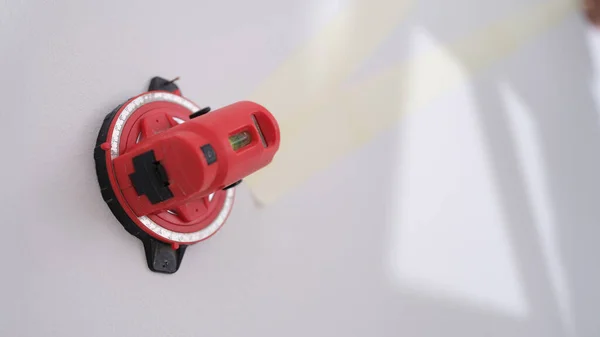 Close-up of red construction laser level fixed on white wall. Professional measuring device for marks. Renovation concept