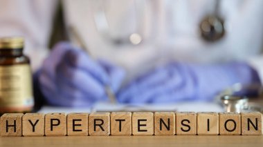 Kelime hipertansiyonu, teşhisi ve tedavisi olan tahta küplere yakın çekim. Doktor tıbbi belgeleri dolduruyor. Anormal yüksek tansiyon