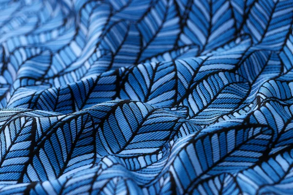 Close-up of blue crumpled fabric with leaves print textured background. Foliage seamless pattern backdrop