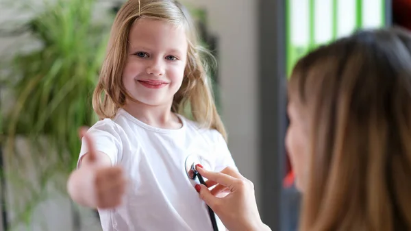 Lekarz Słucha Dziecka Stetoskopem Dziewczyna Trzyma Kciuki Górze Wysokiej Jakości — Zdjęcie stockowe