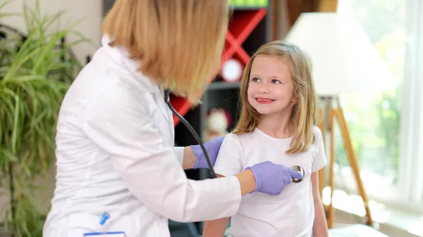 Portrait of doctor pediatrician examines little girl with stethoscope. Small smiling kid at doctor appointment. Healthcare, pediatrics and medicine concept