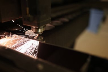 Metal kesme işlemine yakın çekim ve ateş kıvılcımları uçuşuyor. Lazer kesme makinesi, metal levha ve ateşli parçacıklar. Üretim ve üretim kavramı