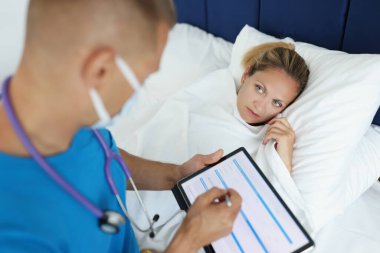 Portrait of doctor making prescription for ill woman, examining of patient. Practitioner typing on modern tablet. Sick female in bad. Healthcare and medicine concept