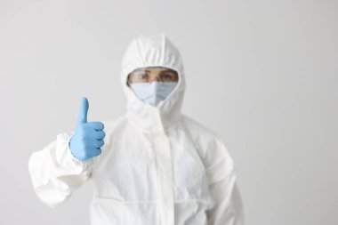 Portrait of woman in protective respirator and white coverall showing thumb up sign. Smart scientist. Female chemist in eyeglasses. Science and lab concept