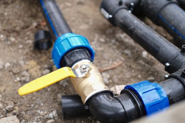 Close-up of elbow fitting of pvc pipes at bend with yellow faucet. Underground irrigation system and plumbing water drainage installation
