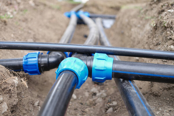 Close-up of plumbing water drainage or underground irrigation system. Elbow fittings and pvc pipes at bend in trench outdoors