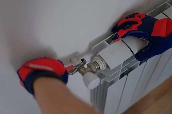 Close-up of male plumber installing heating radiator using pipe wrench. Builder installs new hot water central heating system using wrench. Renovation concept