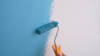 Close-up of decorator painting wall in blue color, interior decorating. Painting walls with roller. Repair and renovation concept