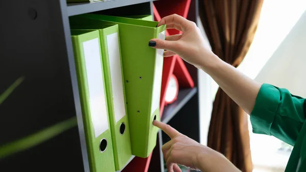 Close-up of woman hands taking off green paper folder. Archive, paperwork and office work Business and workplace organization concept