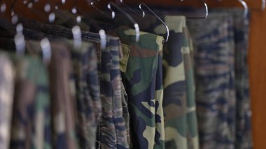 Close-up of collection of military uniform trousers in wardrobe. Camouflage military clothes concept