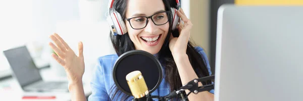 Woman radio presenter laughs in the studio at the microphone, close-up. Radio transmission equipment, joy in the workplace