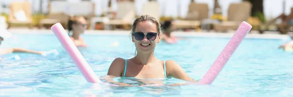 A woman is engaged in aqua fitness in an outdoor pool, close-up, blurry. Aqua aerobics, clear blue water
