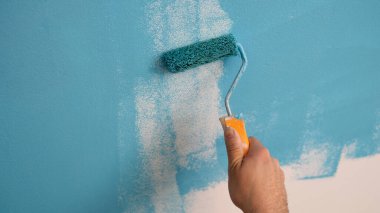 Close-up of decorator hand painting walls in blue color with roller. Interior decorating. Repair and renovation concept