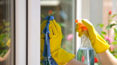 Close-up of woman applying detergent spray and rag for cleaning window outside. House cleaning, housekeeping and spring-cleaning concept
