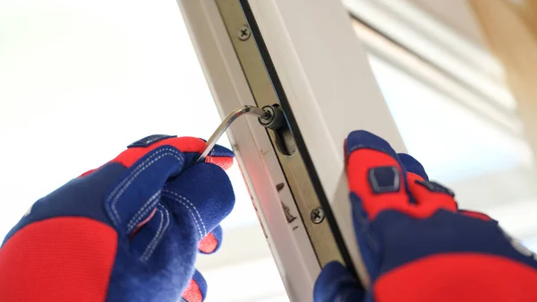 Close-up of repairman hands in gloves adjusting locks of new pvc windows with special key. Installation of plastic windows