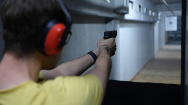 Close-up of male shooter in headphones aiming pistol at target in shooting range. Shooting practicing with gun in rifle range. Extreme hobby concept