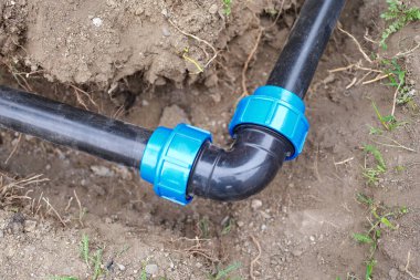 Close-up of elbow fitting and black pvc pipes at bend in trench outdoors. Plumbing water drainage installation. Underground irrigation system concept