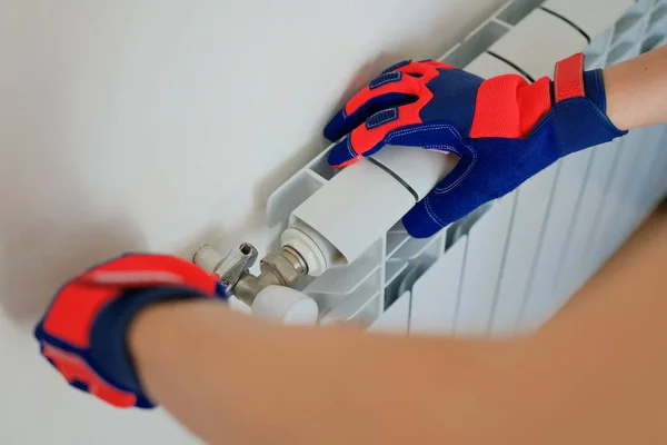 Close-up of male plumber hands in protective gloves installing heating radiator in apartment or house. Builder installs new hot water central heating system using wrench