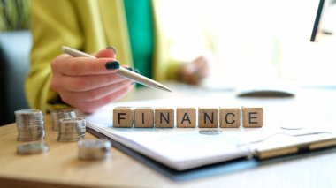 Close-up of woman pointing on word finance made of wooden cubes in row. Business accounting concept