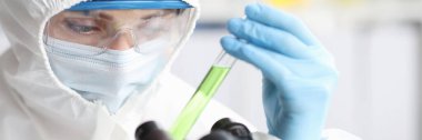 Koruyucu kıyafetli bilim adamı zehirli sıvıyla test tüpü tutuyor. Tehlikeli kimyasallar..