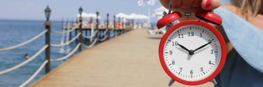 Çalar saat sabah 10 'da kadın eliyle denizin arka planına karşı. Deniz konsepti üzerine güneş saati