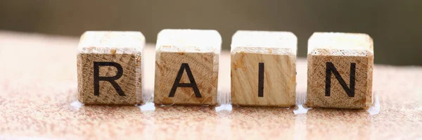 Wooden cubes with words rain lying on wet windowsill closeup. Weather forecast concept