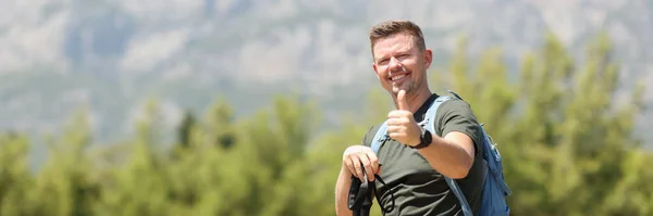 山を背景に北欧の歩行棒を持つ笑顔の男 健康的な勧告とジェスチャー親指アップOkコンセプト — ストック写真